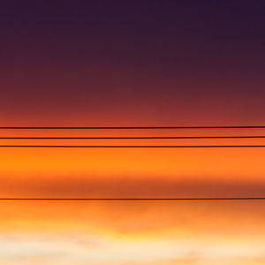 Low angle view of silhouette cables against cloudy orange sky during sunset