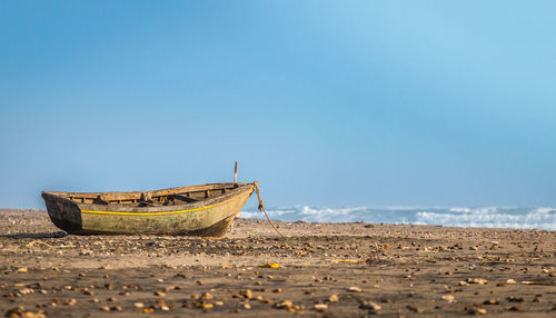 Boat moored at beach against blue sky