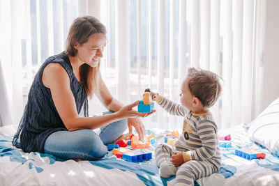 Mother and baby toddler playing building with learning toy stacking blocks at home. 