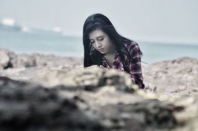 Young woman on rock at beach against sky
