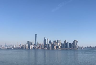 Sea by modern buildings against clear blue sky