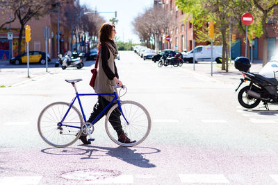 Young smiling woman walking on a city street with bicycle