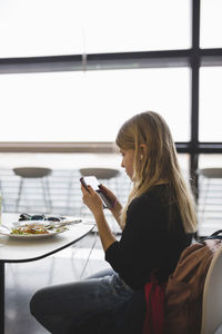 Side view of girl using digital tablet while sitting at table in restaurant