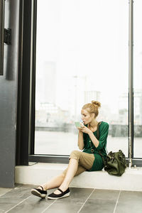 Woman applying lipstick while sitting on window sill at railroad station