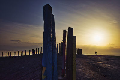 Wooden posts on beach against sky during sunset