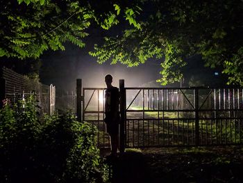 Silhouette man standing by railing against trees at night
