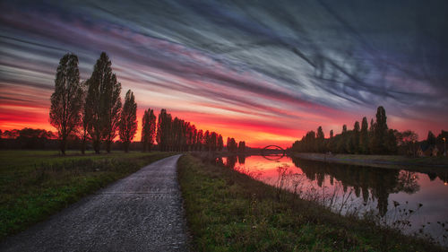 Road by silhouette trees against sky during sunset