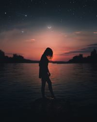 Silhouette woman standing on shore against sky during sunset