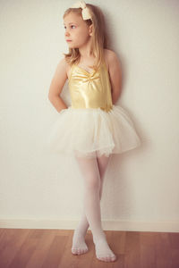 Ballet dancer standing on wooden floor against wall