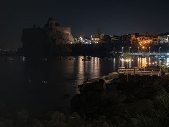 Illuminated buildings by river against sky at night