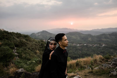 Young man standing on mountain against sky during sunset