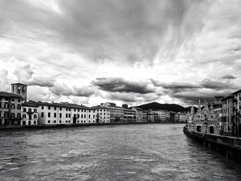 View of city at waterfront against cloudy sky