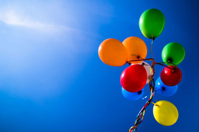 Low angle view of colorful helium balloons against sky