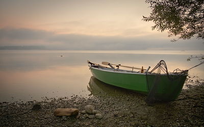 Boat moored on beach against sky during sunset