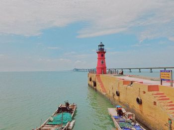 Lighthouse amidst buildings by sea against sky