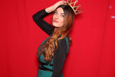 Portrait of young beautiful woman wearing crown standing against red background