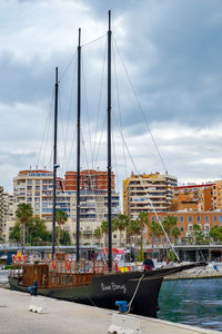 Sailboats moored at harbor against sky in city