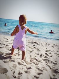 Full length rear view of baby girl standing on sand at beach against sky