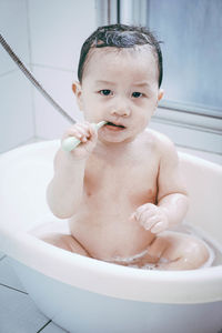 Portrait of baby boy with toothbrush sitting in tub