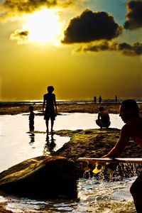 Silhouette people on beach against sky during sunset