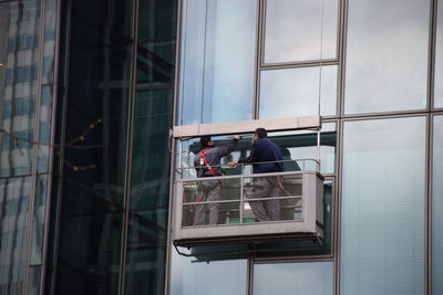 Low angle view of window washers cleaning glass building