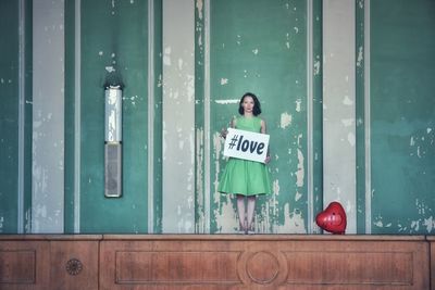 Woman holding love text while standing against wall