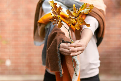 Midsection of woman holding dry leaves against wall