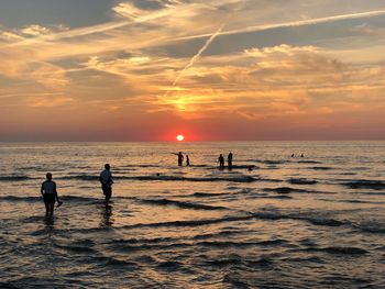 Silhouette people on beach against sky during sunset