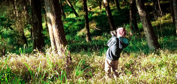 Woman standing by tree on field in forest