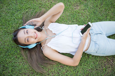 Directly above shot of happy woman listening music while lying on grass