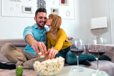 Woman kissing man while sitting on sofa at home