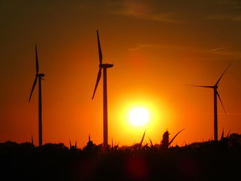 Silhouette wind turbines on field against sky during sunset