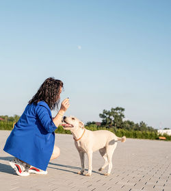 Side view of woman with dog on footpath against clear sky