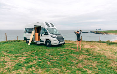 Young woman closing the zipper of her wetsuit for surfing next to her camper van