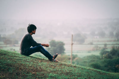 Side view of man sitting on land against sky