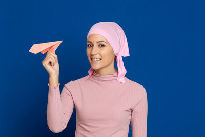 Portrait of smiling young woman holding paper airplane against blue background