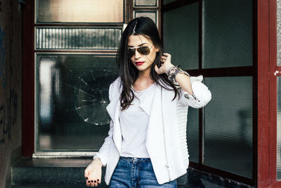 Beautiful woman with hand in hair standing against windows