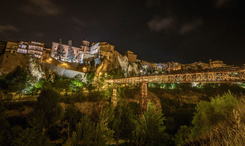 Illuminated buildings by river against sky at night