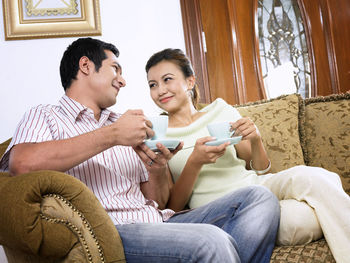 Smiling mid adult couple drinking coffee on sofa at home