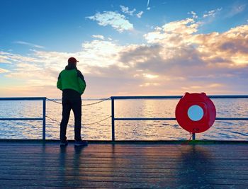 Alone man on pier and look over handrail into water. sunny sky. vivid and strong vignetting effect