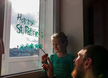 Girl writing on window with father at home