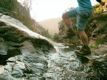 Low section of boy jumping on rocks in river