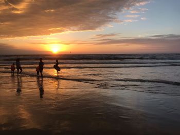 Silhouette people on beach against sky during sunset