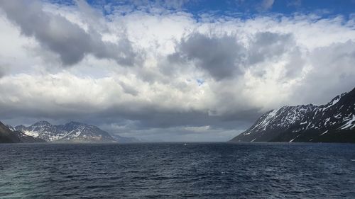 Scenic view of sea by snowcapped mountains against sky