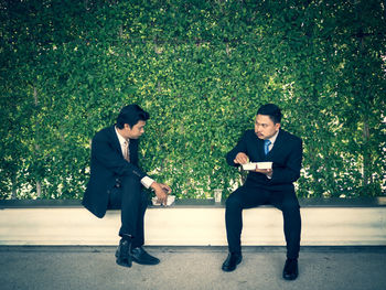 Full length of business people having food while sitting by plants