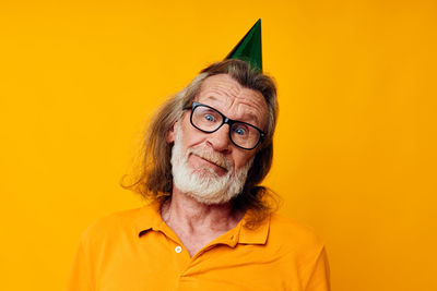 Portrait of senior man wearing party hat against yellow background