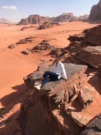 Man sitting on rock at shore against sky