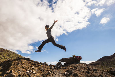 Low angle view of woman jumping on rock against sky