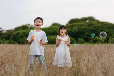 Portrait of happy siblings with bubble wands standing on grassy field