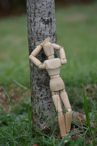 A wooden mannequin leaning on the tree trunk